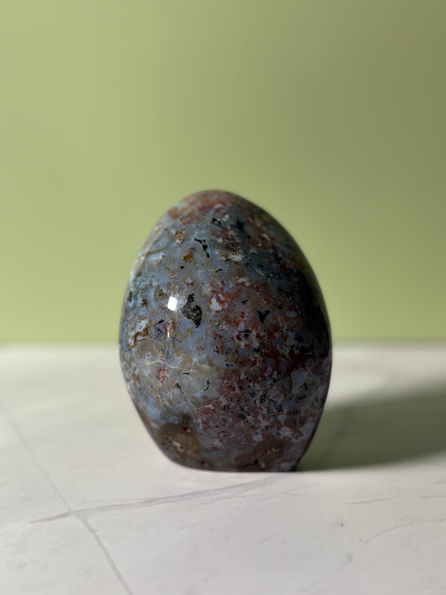Polished sea jasper freeform with blue-gray base and red, black, and golden mineral inclusions.