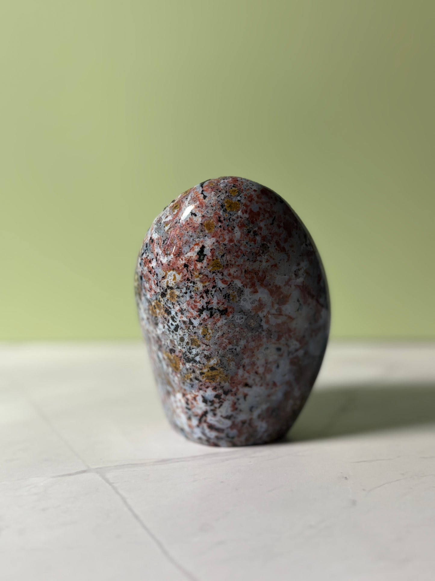 Polished sea jasper freeform with blue-gray base and red, black, and golden mineral inclusions.