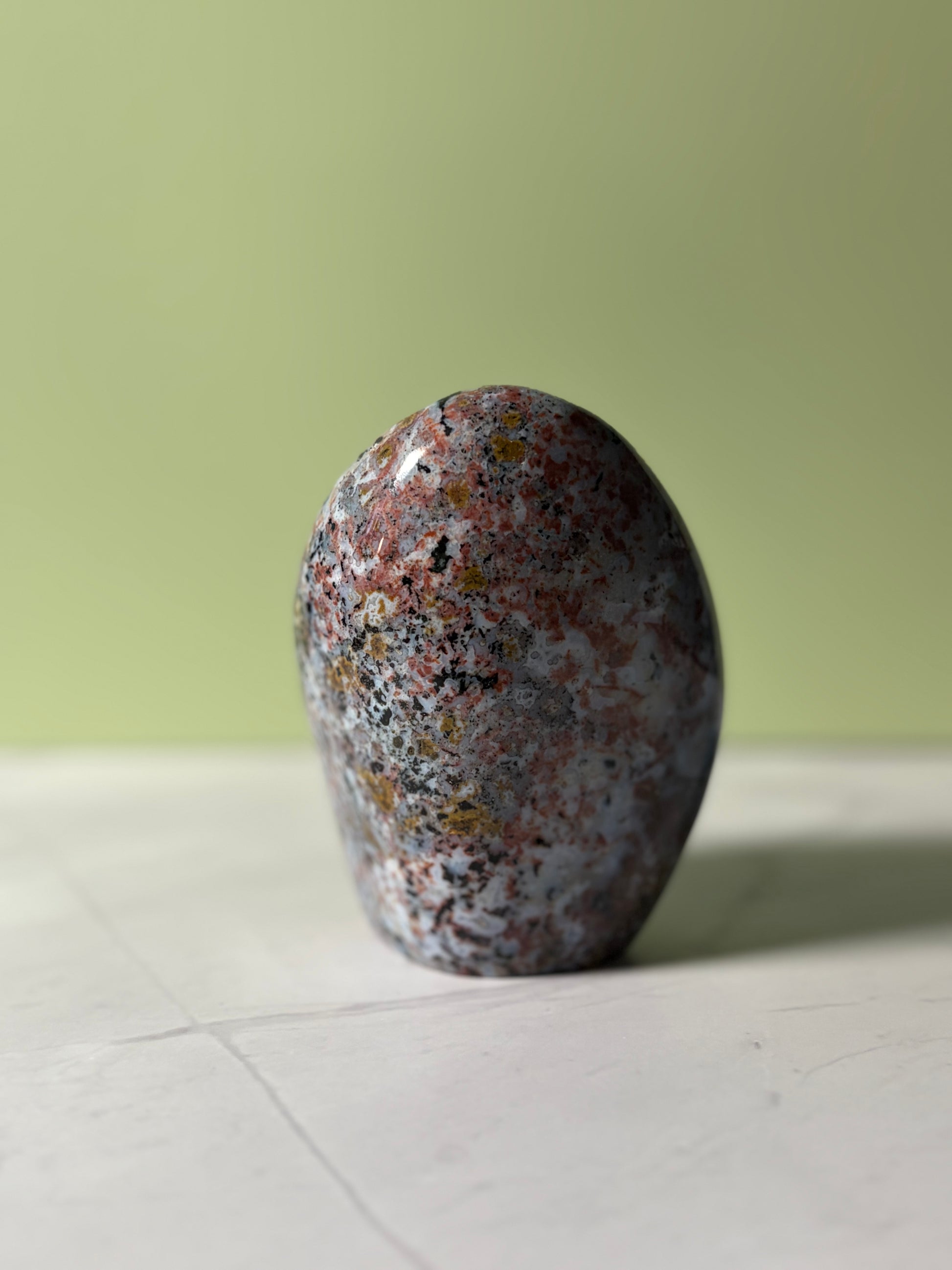 Polished sea jasper freeform with blue-gray base and red, black, and golden mineral inclusions.
