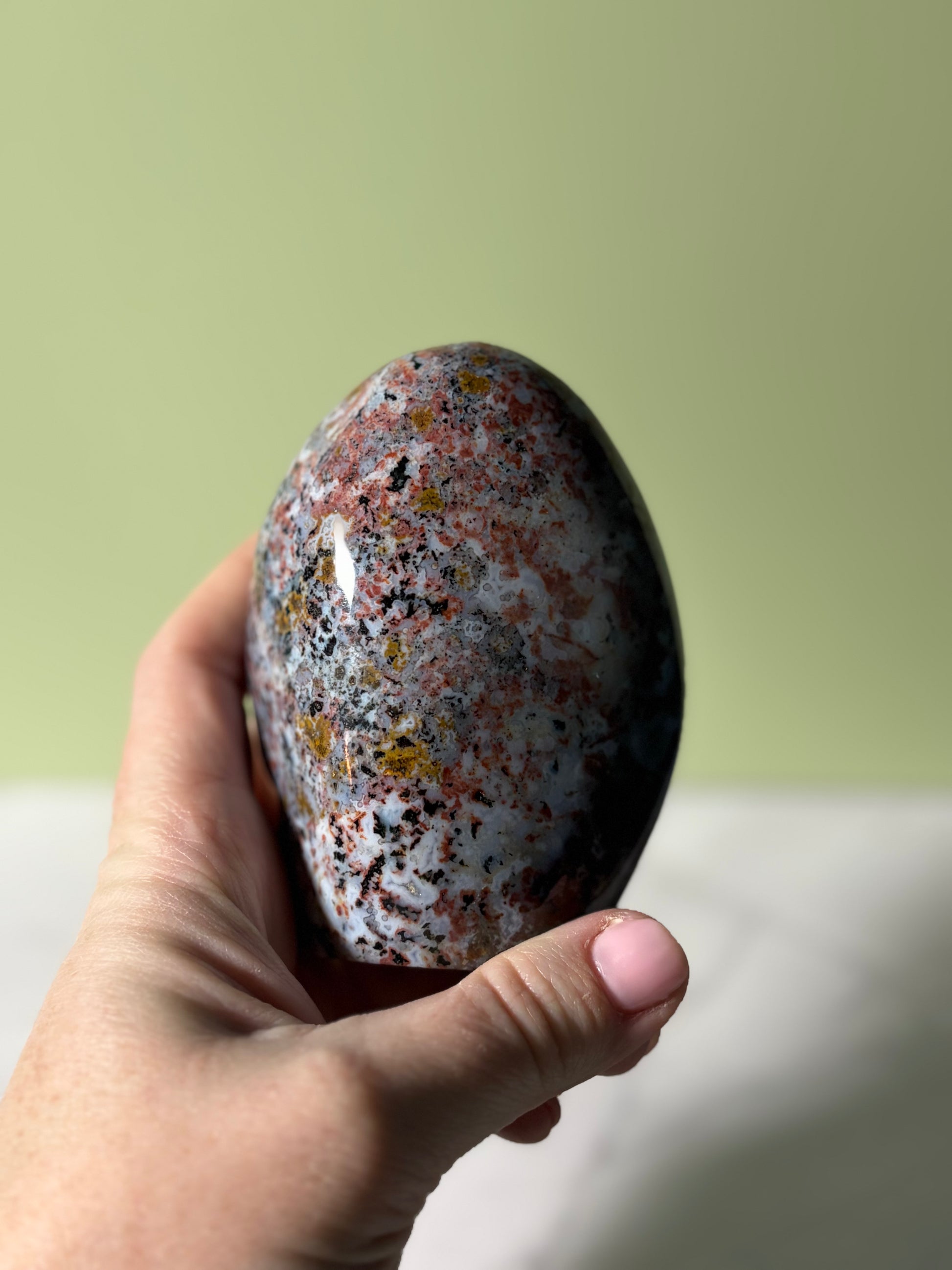Hand holding Polished sea jasper freeform with blue-gray base and red, black, and golden mineral inclusions.