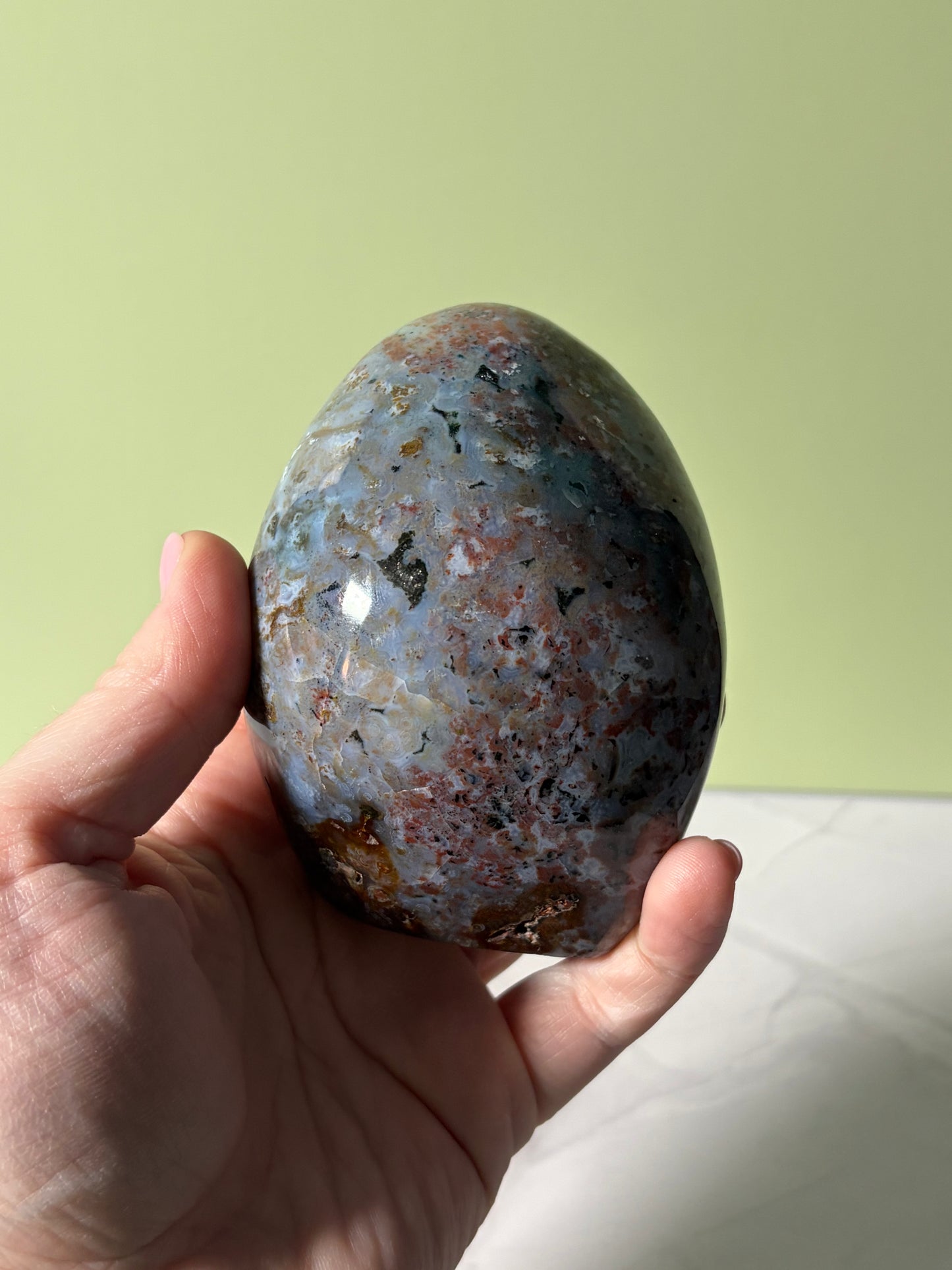 Hand holding Polished sea jasper freeform with blue-gray base and red, black, and golden mineral inclusions.