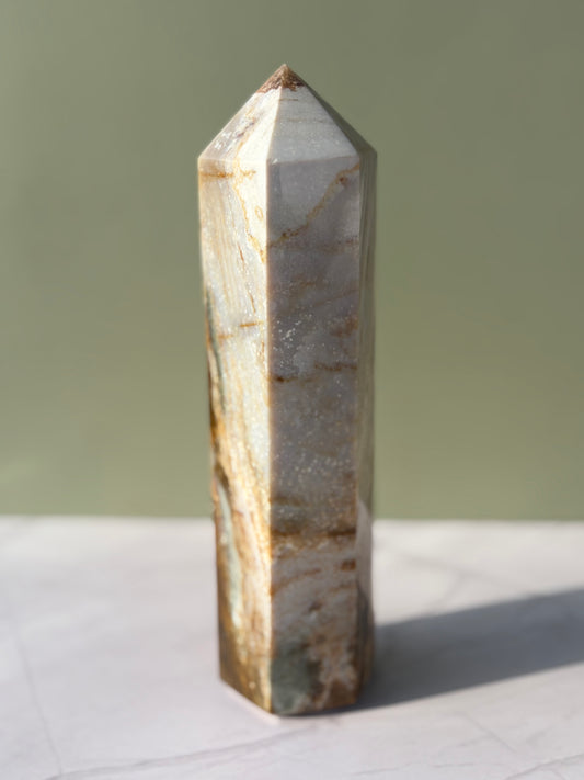 Polished sea jasper tower with soft cream and beige banding photographed on marble surface.