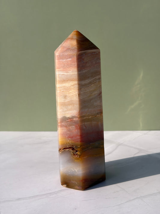 Banded sea jasper tower with soft cream, peach, and golden layers on marble surface.